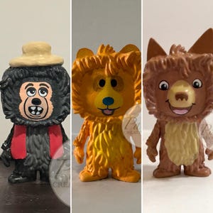 May include: Three hand-painted figurines of cartoon animals. The first is a black monkey wearing a hat and scarf. The second is an orange lion. The third is a brown fox with pointed ears. All have smiling faces.