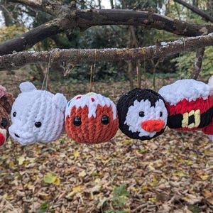 May include: Six crocheted Christmas ornaments hanging from a tree branch. The ornaments are shaped like a reindeer, a polar bear, a gingerbread man, a penguin, Santa Claus, and a snowman.