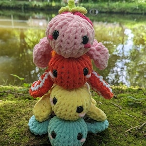May include: A stack of four crocheted turtle toys. The turtles are pink, orange, yellow, and blue. They are stacked on top of each other, with the pink turtle on top.