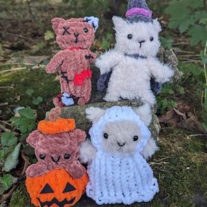 Könnte beinhalten: Vier handgefertigte Plüschtiere zum Thema Halloween. Ein brauner Bär mit genähten Wunden, eine weiße Katze mit einem lila Hexenhut, ein brauner Bär mit einem Kürbis-Kostüm und ein weißes Schaf mit einer weißen Kapuzenrobe.