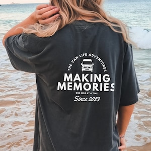 May include: A black t-shirt with a white graphic design featuring a van and the text "The Van Life Adventures Making Memories One Mile at a Time Since 2023".