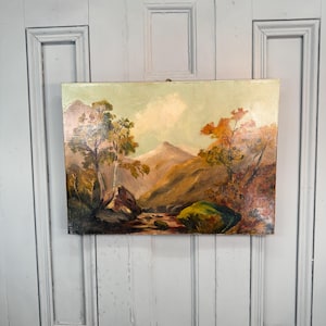 Pode incluir: Uma pintura a óleo sobre tela retratando uma paisagem com uma cordilheira central, um riacho em primeiro plano e árvores com folhagem em tons de outono em laranja, castanho e verde sob um céu pálido e de cores claras.