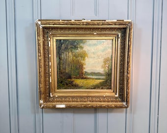 May include: An antique landscape painting in a gold ornate frame. The artwork depicts a serene scene with trees, a field, and a body of water under a cloudy sky. The frame has intricate detailing and shows signs of age.