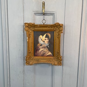 May include: A framed portrait of a woman wearing a yellow and white bonnet. The portrait is in a gold frame with ornate details.