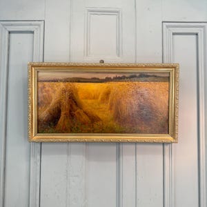 May include: An antique framed painting depicting a wheat field with golden haystacks under a warm, yellow sky. The artwork is encased in a gold ornate frame, adding a touch of vintage charm to the pastoral scene.