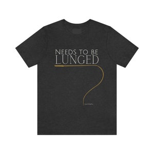 May include: A dark heather grey t-shirt with the text "Needs to be Lunged" in white and a brown whip illustration.