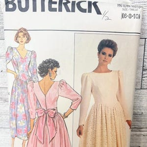 May include: A vintage Butterick sewing pattern with illustrations of dresses. The pattern shows a pink dress with a bow, a floral dress, and a cream-colored dress. The pattern size is (6-8-10).