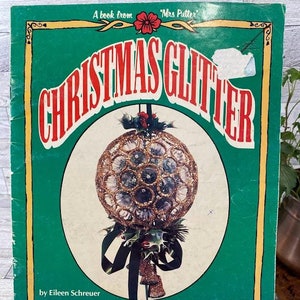 May include: A green book titled "Christmas Glitter" with a red and gold ornament on the cover. The book is by Eileen Schreuer and includes a fun and fancy collection of holiday decorations using glitter and general craft supplies. It also includes projects for year-round holidays and decorating. #7463