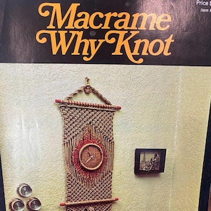 May include: A book titled "Macrame Why Knot" with a picture of a macrame wall hanging with a clock in the center. The wall hanging is made with natural colored cord and red accents. The book is part of a series called "Handy Craft Pak" books.