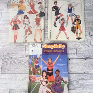 May include: Three sewing pattern envelopes for cheerleader outfits. One McCall's pattern, one Simplicity pattern labeled 8782, and one Simplicity pattern labeled 8294 titled Team Spirit. Each envelope displays illustrations of various cheerleading uniforms.