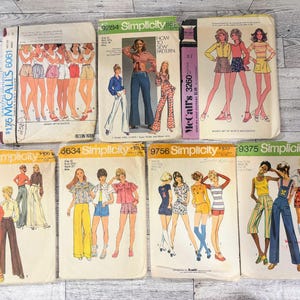 Può includere: Una collezione di sette buste di cartamodelli vintage McCall's e Simplicity, con illustrazioni di vari stili di abbigliamento, inclusi pantaloni a zampa, pantaloncini, gonne e top, con numeri di modello e prezzi stampati.