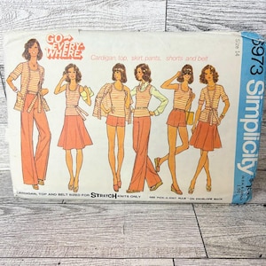 May include: Vintage Simplicity sewing pattern envelope featuring illustrations of a cardigan, top, skirt, pants, shorts, and belt. The envelope is white with orange and brown illustrations, and the text "GO EVERYWHERE" is visible.