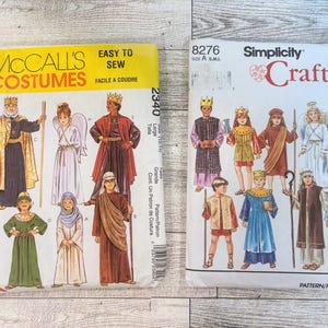 May include: Two vintage costume sewing patterns. One is McCall's Costumes, with illustrations of biblical figures. The other is Simplicity Crafts, also featuring costume designs. Both patterns are on a light-coloured surface.