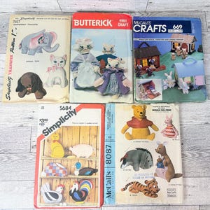 Puede incluir: Una colección de patrones de costura vintage con juguetes de animales, manualidades y figuras de peluche. Los patrones incluyen diseños para un elefante, un gato, un perro, muñecas de gato, una casa en miniatura y personajes de Winnie the Pooh.