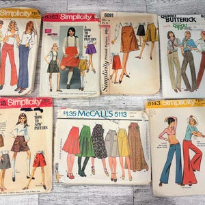 May include: A collection of six vintage sewing pattern envelopes from Simplicity, Butterick, and McCall's. Each envelope features illustrations of various clothing styles including skirts, trousers, and tops, with printed brand names and pattern numbers.