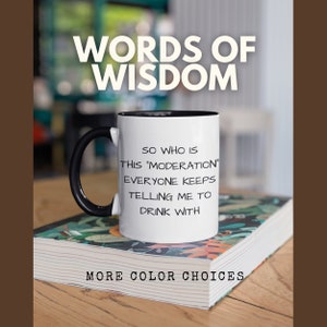 Może przedstawiać: Biały kubek do kawy z czarnym uchwytem i czarnym rantem. Kubek ma zabawny napis: "Więc kto to jest ta "umiarkowanie", o której wszyscy mówią, żebym pił z nią". Kubek stoi na stosie książek, na dolnej książce jest napisane "Więcej kolorów do wyboru".