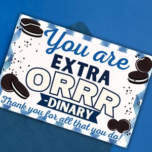 May include: A greeting card with the message "You are EXTRA ORRRDINARY" on a white background with blue accents and Oreo cookie illustrations. The card is placed on a blue envelope, all against a blue backdrop.