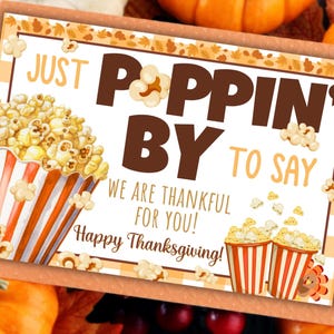 May include: Thanksgiving-themed card with popcorn illustrations and the message "Just Poppin' By To Say We Are Thankful For You! Happy Thanksgiving!" in brown and orange. The card has a decorative border and is set against a background of pumpkins.