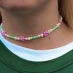 May include: A white pearl choker necklace with pink and green flower-shaped beads.