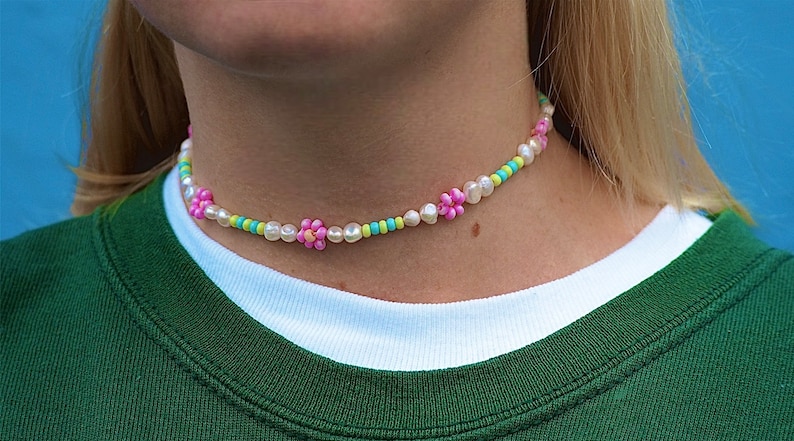 May include: A white pearl choker necklace with pink and green flower-shaped beads.