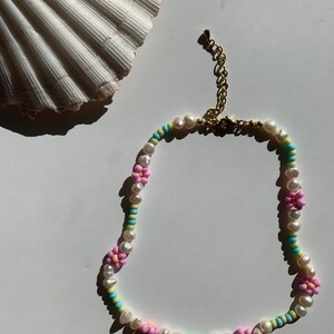 May include: A delicate pearl and flower bead necklace with a gold clasp. The necklace features pink, blue, and yellow flower beads interspersed with white pearls.