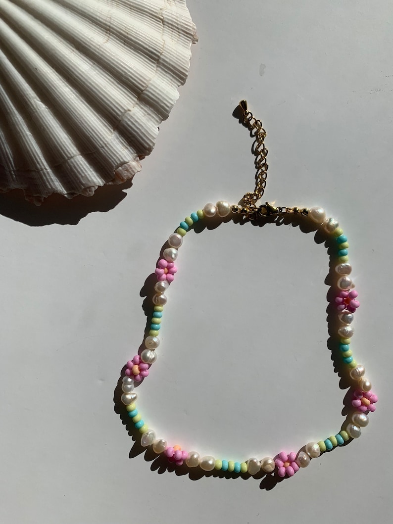 May include: A delicate pearl and flower bead necklace with a gold clasp. The necklace features pink, blue, and yellow flower beads interspersed with white pearls.