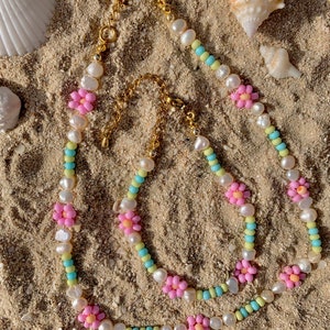 May include: Three layered necklaces with pastel colored beads and pink flower accents. The necklaces are made of white pearls and small beads in shades of blue, yellow, and green.