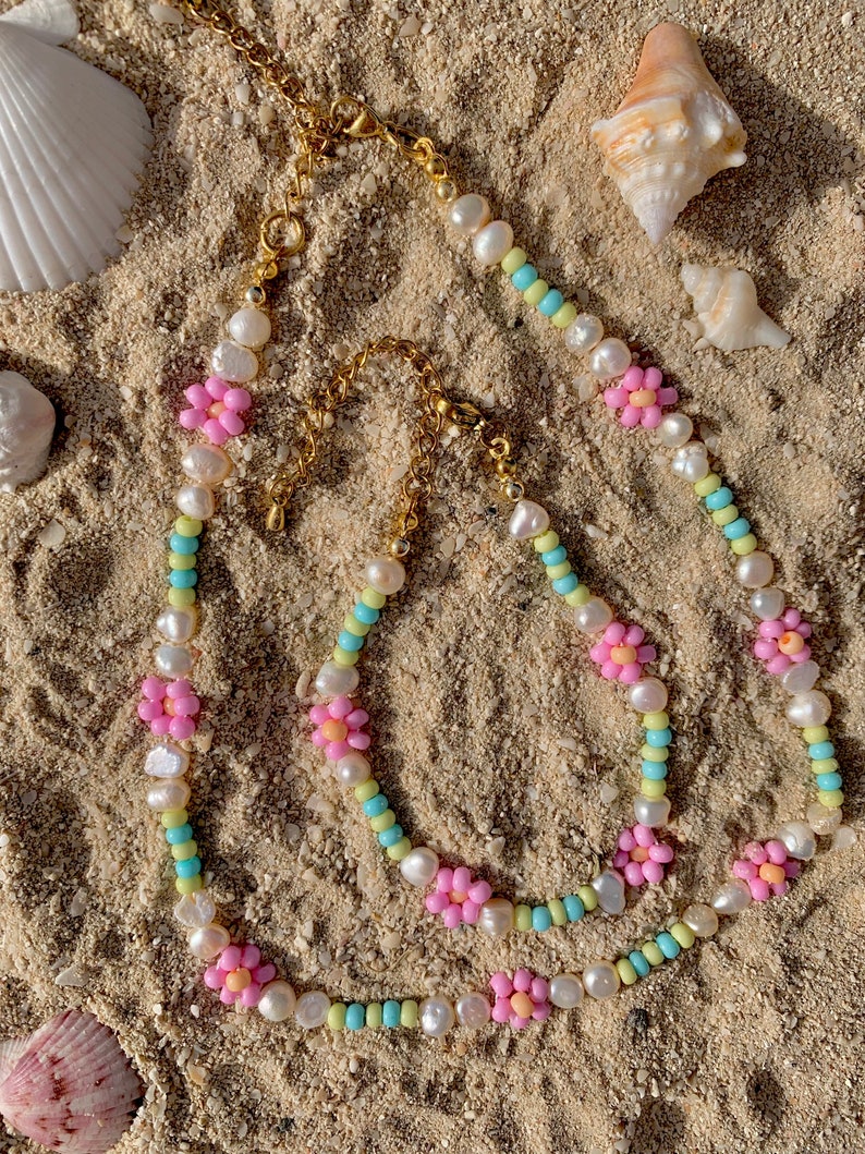 May include: Three layered necklaces with pastel colored beads and pink flower accents. The necklaces are made of white pearls and small beads in shades of blue, yellow, and green.