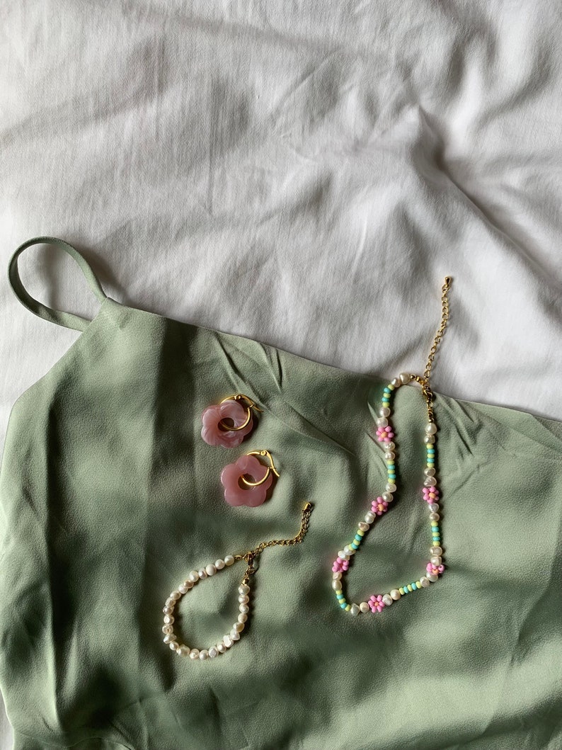 May include: A set of pink flower-shaped earrings, a pearl bracelet, and a beaded necklace with pink and green flowers. The jewelry is on a green fabric background.