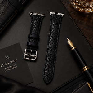 Peut inclure: Un bracelet de montre noir avec un motif texturé en peau de serpent, doté de connecteurs en métal argenté et d'une boucle assortie. Le bracelet se compose de deux parties, l'une avec une boucle et deux passants, l'autre avec une extrémité pointue.