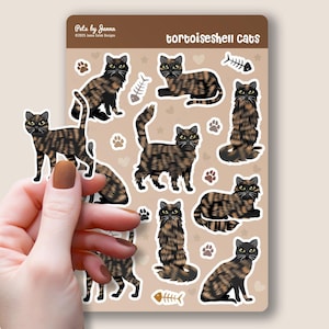 May include: A sheet of stickers featuring tortoiseshell cats in various poses. The stickers are on a brown background with paw prints, hearts, stars, and fish bones. The text "tortoiseshell cats" is at the top of the sheet.