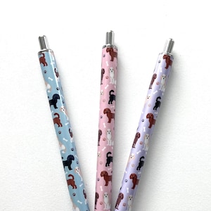 May include: Three pens with different colored backgrounds and a pattern of dogs and bones. The pens are silver with a silver clip.