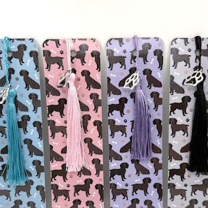 May include: Four rectangular bookmarks with dog patterns in blue, pink, purple, and gray. Each bookmark has a tassel and a decorative charm. The tassels are blue, pink, purple, and black.