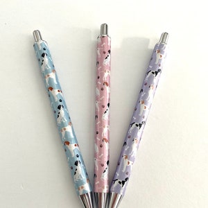 May include: Three pens with silver caps and a pattern of dogs on a light blue, pink, and purple background.
