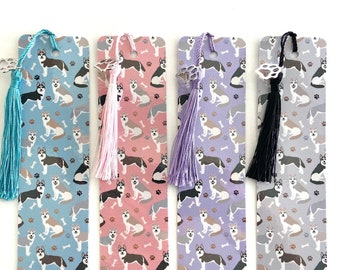 May include: Four bookmarks with a husky dog pattern. The bookmarks are blue, pink, purple, and gray. Each bookmark has a silver charm and a tassel. The tassels are turquoise, pink, purple, and black.