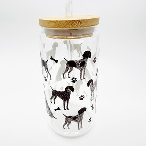 May include: A clear glass tumbler with a bamboo lid and a clear straw. The tumbler is decorated with a repeating pattern of black and gray dog illustrations, paw prints, and bones.