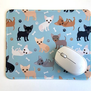 May include: A blue mouse pad with a repeating pattern of white, brown, and black chihuahua dogs. A white wireless computer mouse is on top of the mouse pad.