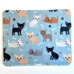May include: A blue mouse pad with a repeating pattern of cartoon chihuahua dogs in various colors and poses. The dogs are on a light blue background with white paw prints.
