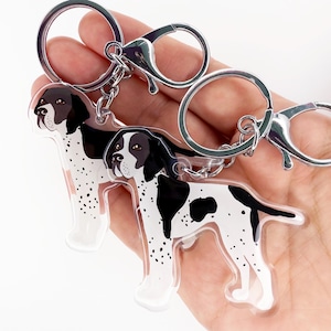 May include: Two clear acrylic keychains featuring a black and white dog design. Each keychain has a silver-colored metal ring and clasp. The dog illustration has black spots and a black head.