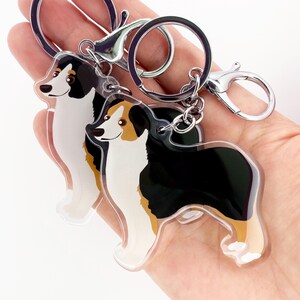 May include: Three acrylic dog keychains featuring a black, white, and tan Australian Shepherd design. Each keychain has a silver-colored clasp and keyring. The keychains are in the shape of a dog.