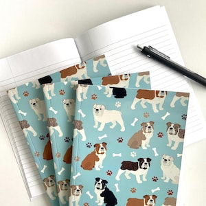 May include: Four blue notebooks with a repeating pattern of brown, white, and black bulldogs on a light blue background. The notebooks have white bones and paw prints scattered throughout the pattern.