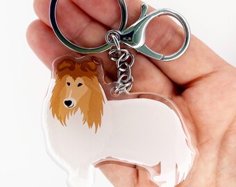 May include: A clear acrylic keychain featuring a cartoon collie dog with a white body and brown fur. The keychain has a silver keyring and clasp. The dog illustration is detailed with a black nose and eyes.