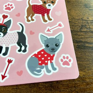 K&ouml;nnte beinhalten: Ein Bogen rosa Sticker mit verschiedenen Illustrationen von Hunden, die rote und wei&szlig;e Pullover mit Herzen tragen. Die Hunde sind in verschiedenen Posen, wie sitzend, stehend und laufend. Die Sticker sind perfekt, um jedem Projekt eine Prise Niedlichkeit zu verleihen.