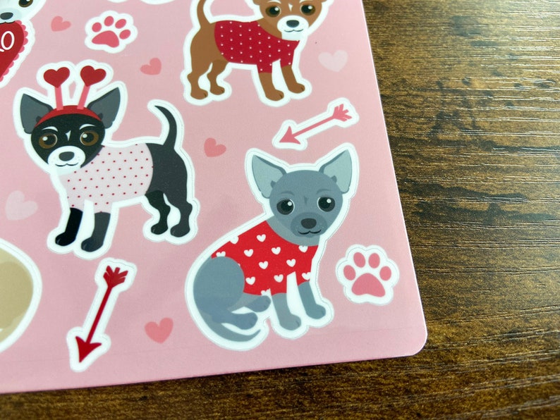K&ouml;nnte beinhalten: Ein Bogen rosa Sticker mit verschiedenen Illustrationen von Hunden, die rote und wei&szlig;e Pullover mit Herzen tragen. Die Hunde sind in verschiedenen Posen, wie sitzend, stehend und laufend. Die Sticker sind perfekt, um jedem Projekt eine Prise Niedlichkeit zu verleihen.