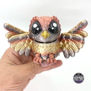 May include: A 3D-printed owl figurine with large, expressive eyes and articulated wings. The owl features a color scheme of bronze, gold, and copper. The figurine is held in a hand, with the "AUTHORIZED SELLER" logo visible.