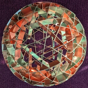 May include: A decorative sphere made of metal with a geometric design. The sphere is made of copper and green metal pieces that are interwoven to create a complex pattern.