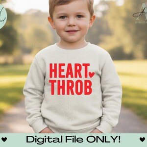 Op de afbeelding: Een kind draagt een lichtbeige sweatshirt met de woorden "HEART THROB" in rode blokletters en een rood hart. De woorden "Digital File ONLY!" staan onderaan de afbeelding. De achtergrond is wazig.