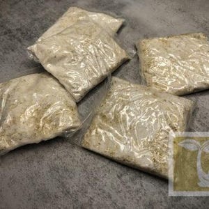 May include: Five clear plastic bags filled with a light brown, grainy substance. The bags are sealed and appear to be ready for packaging.