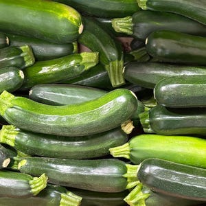 K&ouml;nnte beinhalten: Nahaufnahme eines Stapels frischer, dunkelgr&uuml;ner Zucchini. Die Zucchini sind in einem zuf&auml;lligen Muster angeordnet, wobei sich einige &uuml;berlappen.