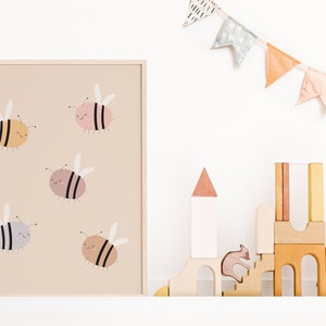 Puede incluir: Una impresi&oacute;n enmarcada con un fondo beige que presenta cinco abejas de dibujos animados en varios colores, incluyendo amarillo, rosa, gris y marr&oacute;n. Las abejas tienen rayas negras y caras sonrientes. La impresi&oacute;n se muestra en un estante blanco con un castillo de juguete de madera y una pancarta de tela.
